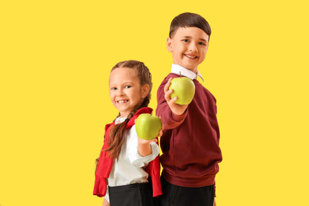 Little schoolchildren with apples on yellow backgroundの写真素材