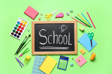 Chalkboard with text SCHOOL and different stationery on green background