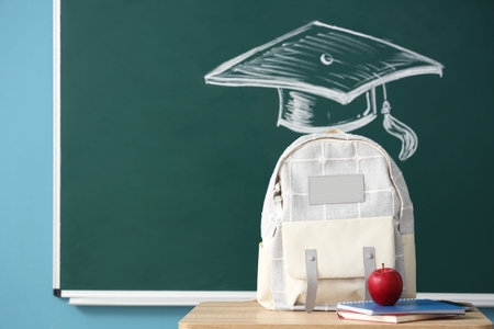 Backpack with apple on desk near blackboard in classroom