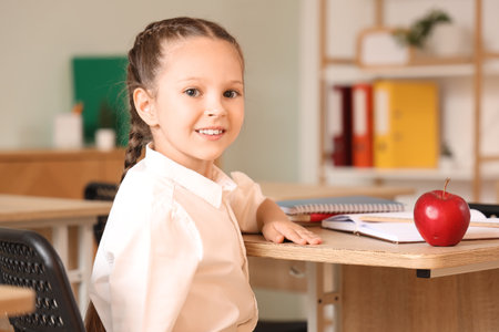 Little schoolgirl with apple at desk in classroomの写真素材