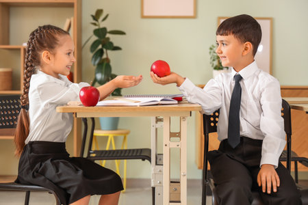 Little schoolgirl taking apple from classmate in classroomの写真素材