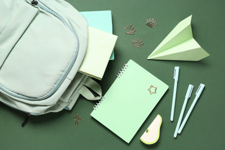 School backpack, paper airplane and different stationery on green background