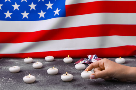 Female hand with burning candles and pinwheel on table against flag of USA. National Day of Prayer and Remembrance for the Victims of the Terrorist Attacksの写真素材