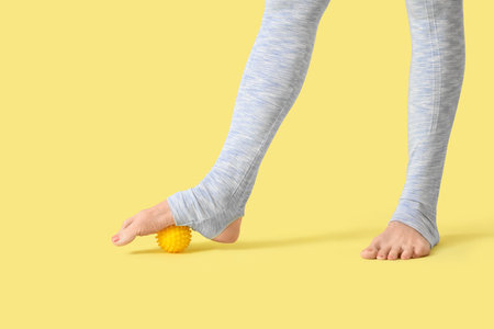 Sporty mature woman massaging her foot with ball on yellow background, closeupの写真素材