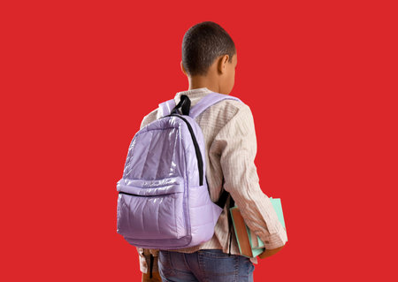 Little schoolboy with backpack and books on red background, back view
