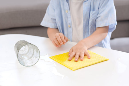 Cute little girl wiping spilled water on table at home, closeup