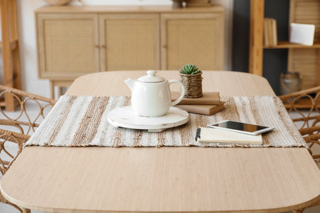 Teapot with tablet computer and books on dining table in roomの写真素材