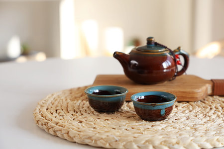 Teapot with cups on dining table in room, closeup