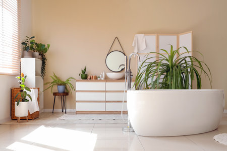 Interior of stylish bathroom with bathtub, chest of drawers, houseplants and mirrorの写真素材