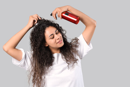 Beautiful young happy African-American woman with hair spray on gray backgroundの写真素材