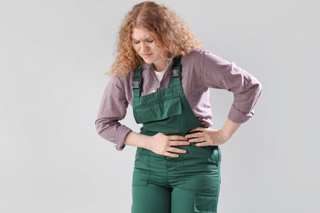 Female worker suffering from menstrual cramps on light backgroundの写真素材