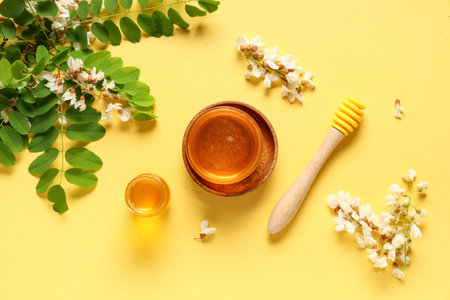 Jars of sweet honey with acacia flowers and dipper on yellow backgroundの写真素材