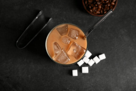 Glass of iced latte with sugar and bowl of coffee beans on black backgroundの写真素材