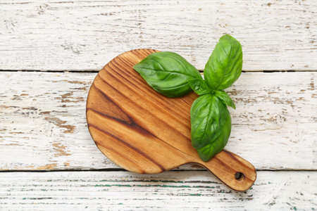Board with fresh green basil leaves on white wooden backgroundの写真素材