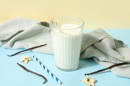 Glass of fresh vanilla milk with sticks and flowers on colorful backgroundの写真素材