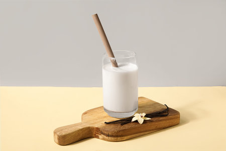 Glass of fresh vanilla milk with sticks and flowers on colorful backgroundの写真素材