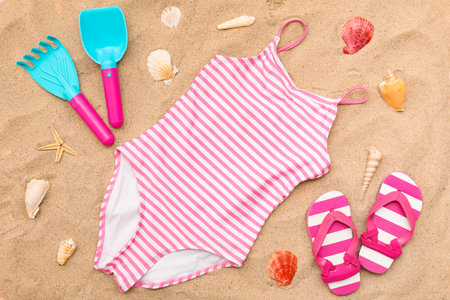Beach accessories for children, flip-flops and swimsuit on sand. Top viewの写真素材