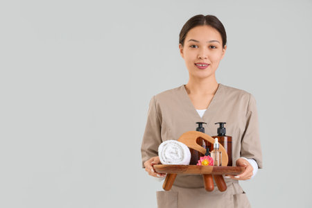 Female Asian massage therapist with spa supplies on light backgroundの写真素材