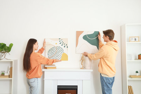 Young couple paintings on wall above fireplace hanging at home, back viewの写真素材