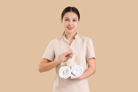 Female Asian massage therapist with herbal bags and towels on beige backgroundの写真素材