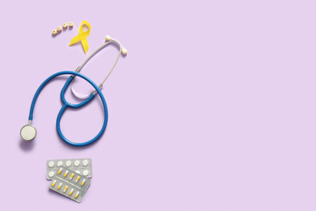 Yellow ribbon, stethoscope, pills and wooden cubes with the word HOPE on lilac background. Sarcoma concept.の写真素材