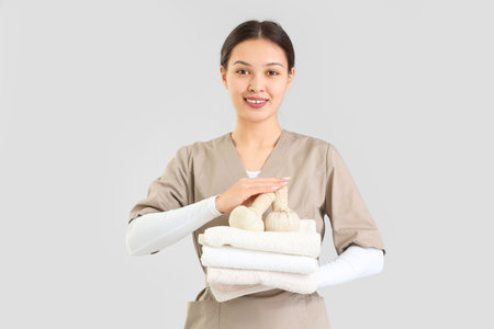 Female Asian massage therapist with towels and herbal bags on light backgroundの写真素材