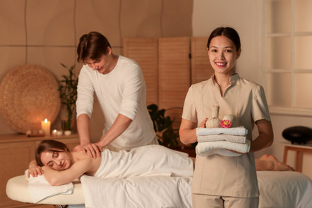 Female Asian massage therapist with towels and herbal bags in dark spa salonの写真素材