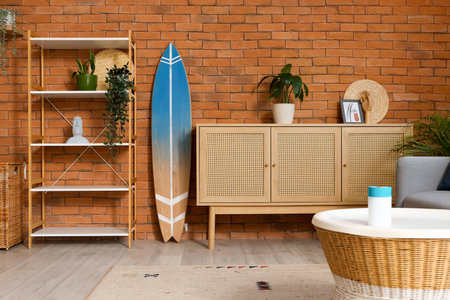 Surfboard, shelving unit and chest of drawers near brown brick wall in beautiful living roomの写真素材