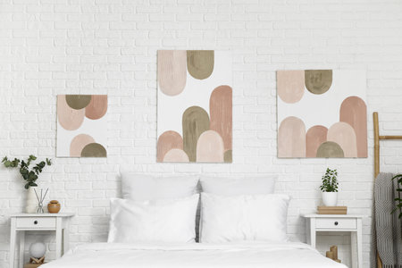 Interior of beautiful bedroom with comfy bed, bedside tables and pictures on white brick wallの写真素材