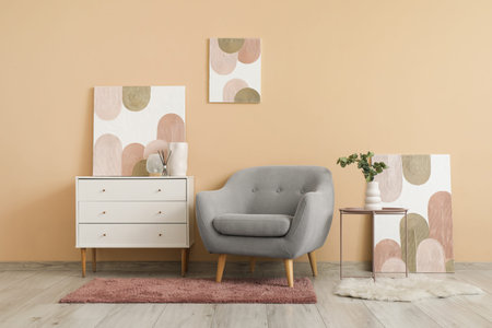 Gray armchair, white chest of drawers and beautiful pictures on beige wall in living room