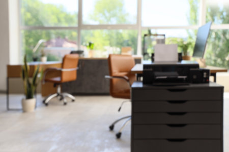 Blurred view of office with desks and printer on drawersの写真素材
