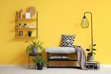 Gray bench, lamp, shelf and houseplants near yellow wall in stylish roomの写真素材