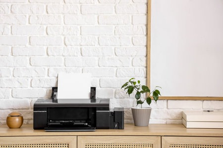 Modern printer with plant on commode near white brick wall in office