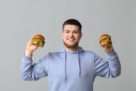 Young man with tasty burgers on gray backgroundの写真素材