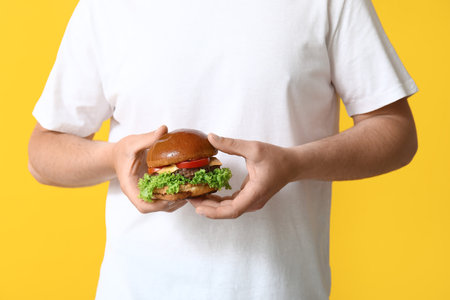 Man with tasty burger on yellow backgroundの写真素材