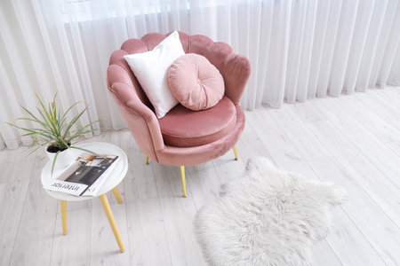 Interior of living room with pink armchair, magazine, cushions, houseplant and coffee table