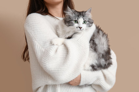Young woman with longhaired adorable cat on beige backgroundの写真素材