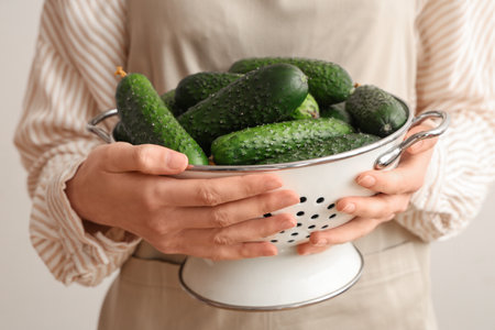 Woman holding colander with fresh green cucumbers on white backgroundの写真素材