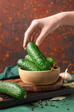 Female hand with wooden bowl of fresh green cucumbers on colorful backgroundの写真素材