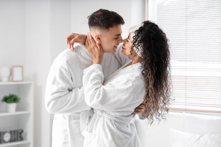 Happy young couple in bathrobes kissing at homeの写真素材