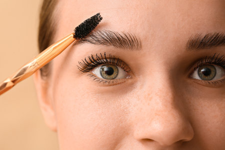 Young woman correcting the shape of her eyebrows on brown background, closeupの写真素材