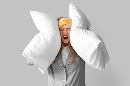 Stressed young woman with pillows suffering from insomnia on light backgroundの写真素材