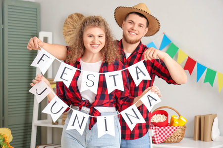Happy young couple holding bunting with text FESTA JUNINA at home