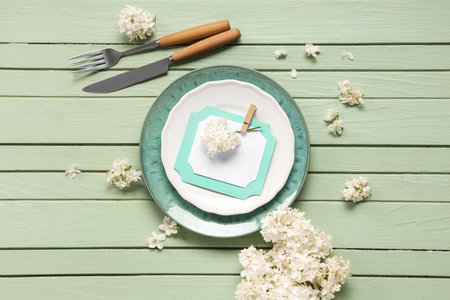 Beautiful table setting with white lilac flowers and invitation on green wooden backgroundの写真素材