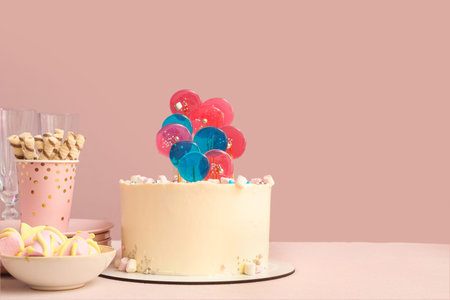 Cake with sweets for birthday party on table against pink wall