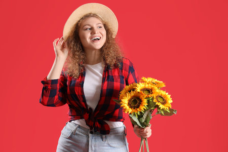 Happy young woman with sunflowers and straw hat on red background. Festa Junina celebrationの写真素材