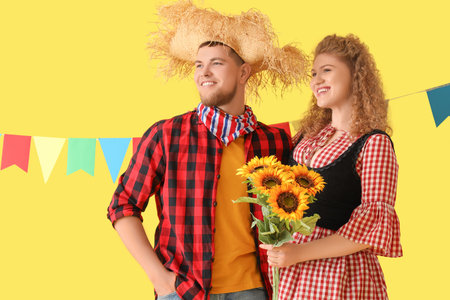 Happy young couple with flags and sunflowers on yellow background. Festa Junina celebration