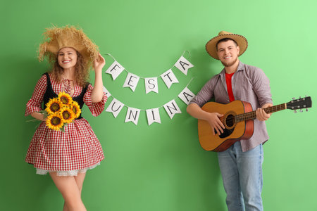 Happy young couple with guitar, sunflowers and FESTA JUNINA bunting on green background