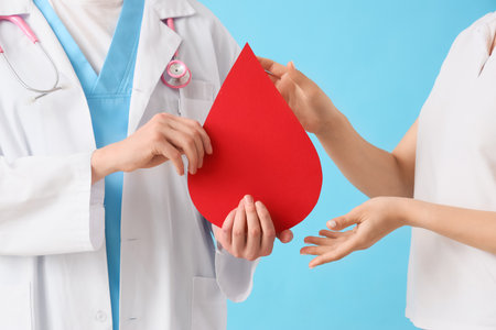 Male doctor giving paper blood drop to woman on blue background, closeupの写真素材
