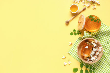 Jars and bowl of sweet honey with acacia flowers on yellow backgroundの写真素材